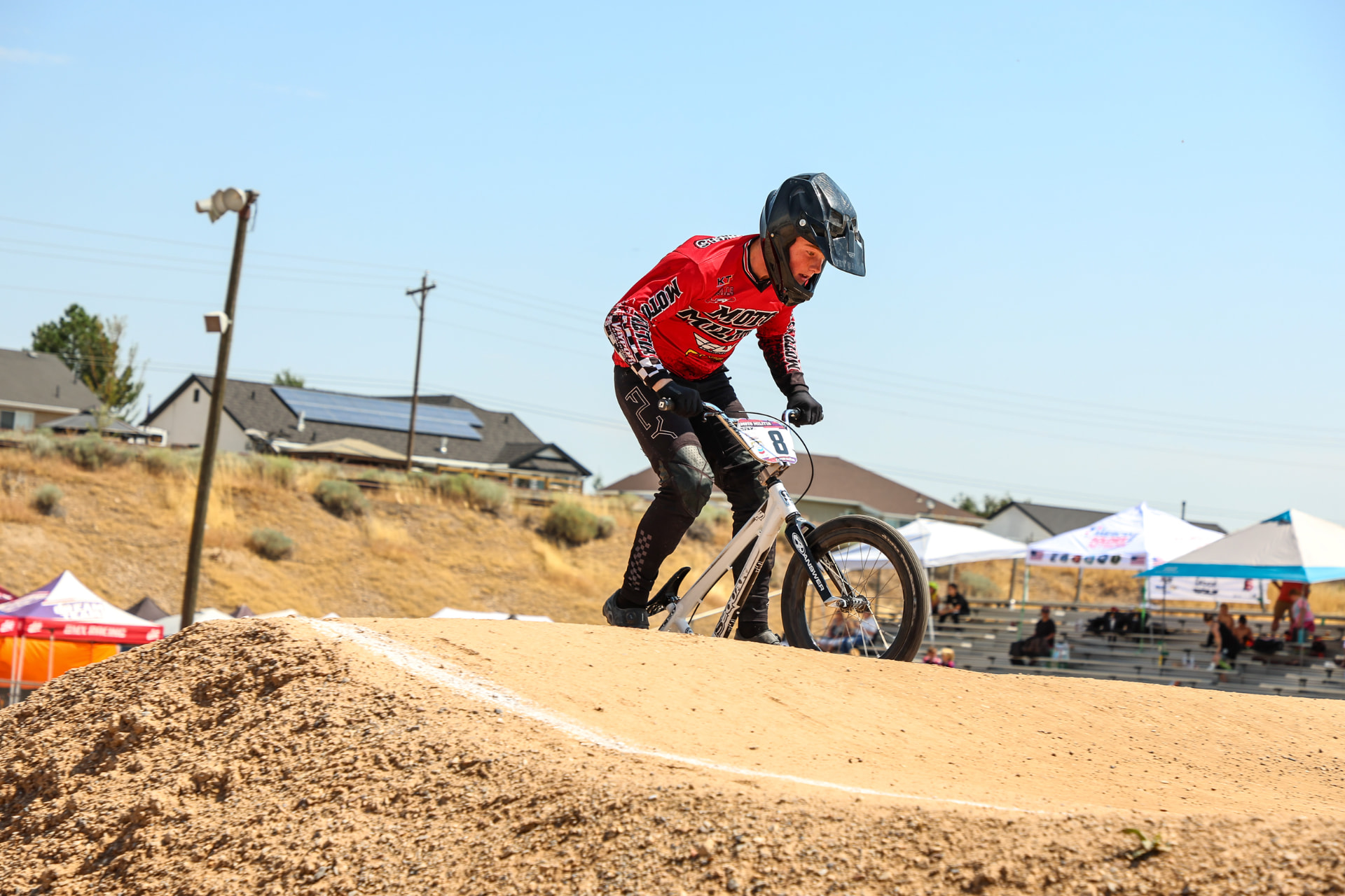 Canyon on his BMX race bike cresting a dirt jump, blue sky behind