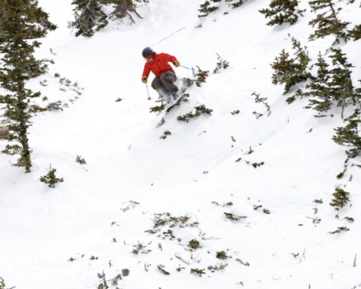 Canyon skiing between evergreen trees in a red jacket